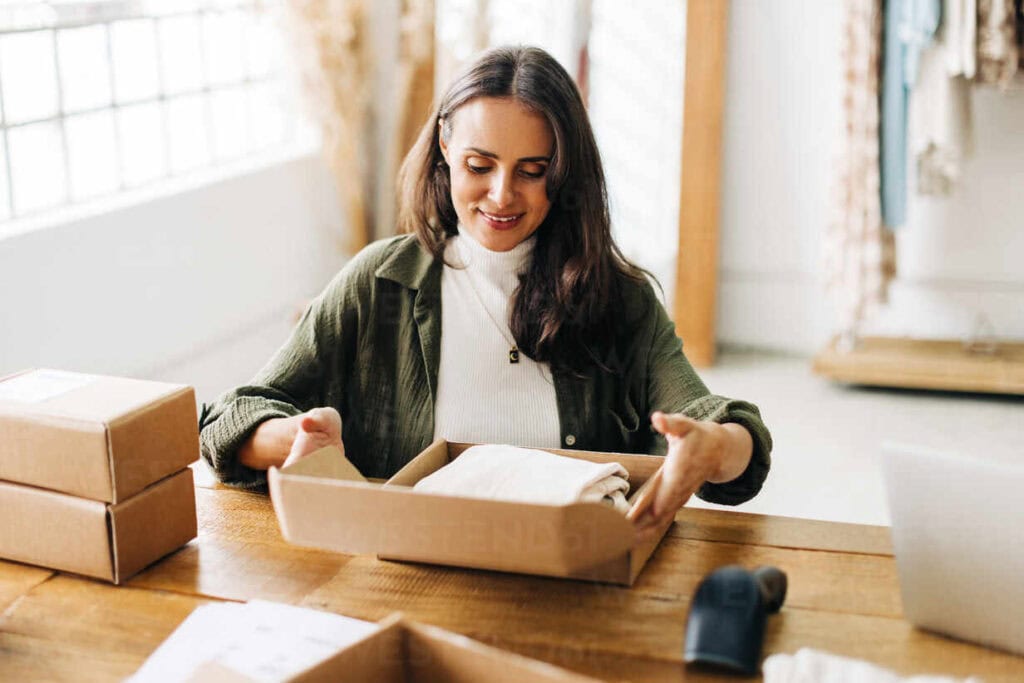 40 Profitable Business Ideas for Women in 2026 – Start Small, Dream Soft, Grow Bold. 1 female online store owner doing order fulfilment in her boutique packaging clothing products into biodegradable boxes woman using dropshipping to run her small business JLPSF30217